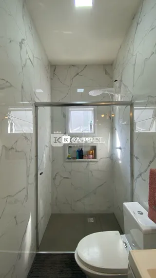 Banheiro com paredes de mármore branco e box de vidro.