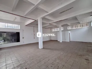 Sala ampla e vazia com piso de cerâmica e estrutura de teto exposta.