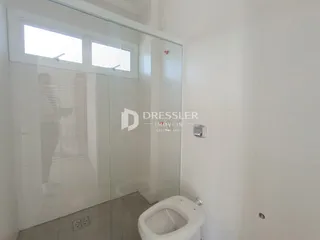 Foto de um banheiro com piso e paredes brancas e divisória de vidro.