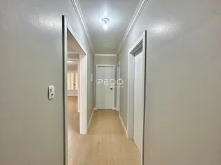 Corredor interno de uma residência com piso de madeira clara e paredes brancas.