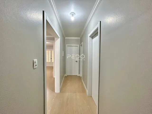 Corredor interno de uma residência com piso de madeira clara e paredes brancas.