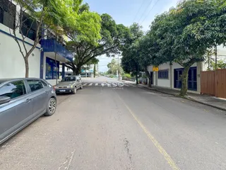 Vista da rua em Lajeado, Brasil, com árvores e veículos estacionados.