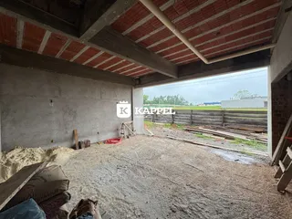 Foto de um espaço interno em construção com teto de madeira exposta e piso de terra.