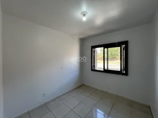 Foto de um cômodo interno com paredes brancas e piso de cerâmica, mostrando uma janela.