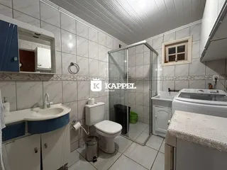 Banheiro com box de vidro, pia e máquina de lavar roupa em ambiente claro.
