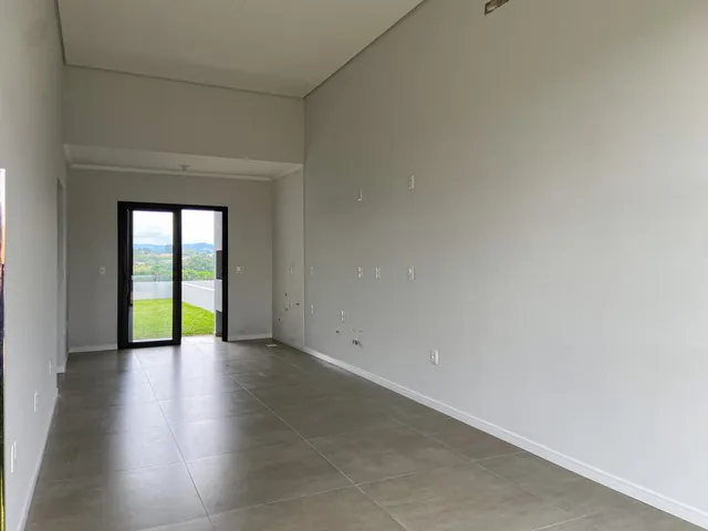Vista interna de um ambiente amplo com piso de porcelanato e porta de vidro que dá para um gramado.
