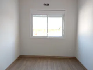 Vista interna de uma sala com paredes brancas e piso de madeira.