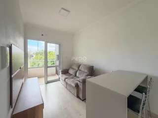 Sala de estar iluminada com sofá e porta de vidro abrindo para a varanda.