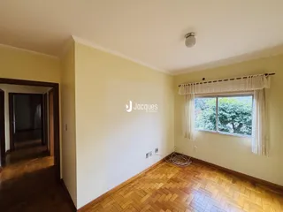 Sala de estar com piso de madeira clara e janela com cortinas brancas.