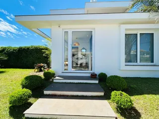 Fachada de uma residência branca com jardim gramado e entrada de vidro.