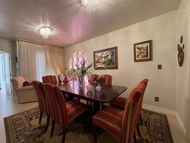 Sala de jantar com mesa de madeira escura e cadeiras estofadas em um ambiente bem iluminado.
