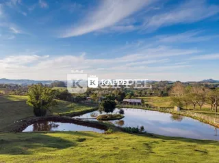 Vista de um campo verde com um lago e vegetação ao fundo.