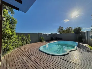 Vista da piscina e deck de madeira em área externa.