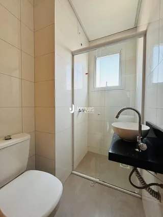 Banheiro com box de vidro e revestimento cerâmico nas paredes.