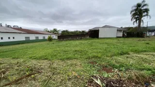 Uma foto externa mostra um terreno gramado com construções ao fundo.
