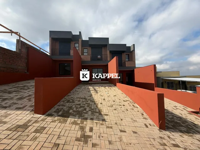A foto mostra a fachada moderna de uma casa com paredes vermelhas e um pátio pavimentado.