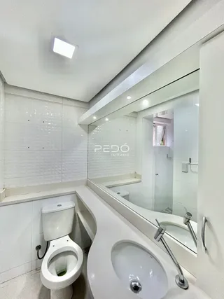 Interior de um banheiro com azulejos brancos e louças sanitárias modernas.
