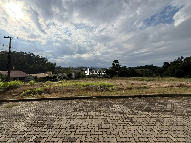 Paisagem de campo com vegetação e área pavimentada na frente da propriedade.