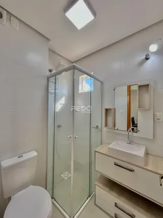 Interior de um banheiro moderno com box de vidro e bancada branca.