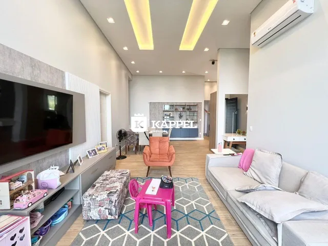 Sala de estar moderna com sofá, televisão e piso de madeira clara.