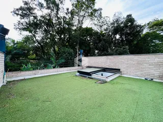 Vista externa de um quintal com gramado verde e muro de tijolos.