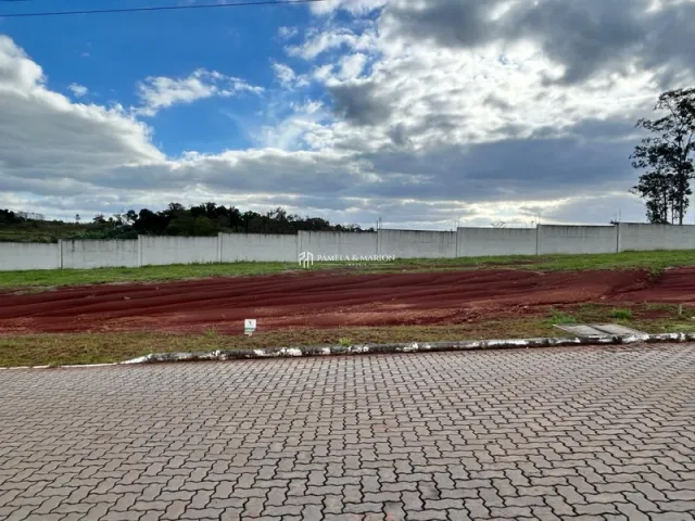 Vista externa de um terreno com terra vermelha e grama sob um céu nublado.