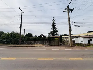 Vista externa de uma propriedade com cerca e vegetação ao lado de uma estrada.