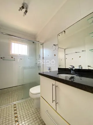 Interior de um banheiro com box de vidro e bancada escura.