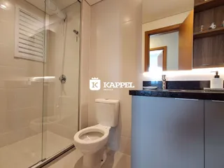 Foto interna de um banheiro com box de vidro e louças brancas.