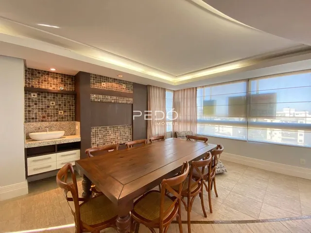 Uma sala de jantar com mesa de madeira e grandes janelões.