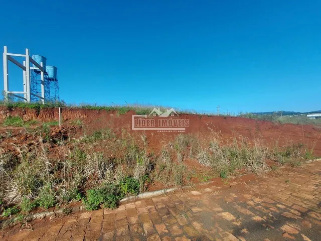 Paisagem de terra vermelha com vegetação seca e uma estrutura metálica ao fundo.