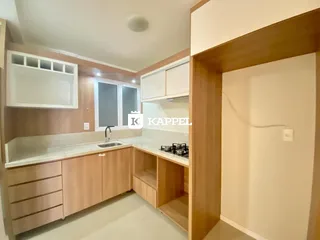 Cozinha com armários de madeira clara e bancada branca em um imóvel em Lajeado.