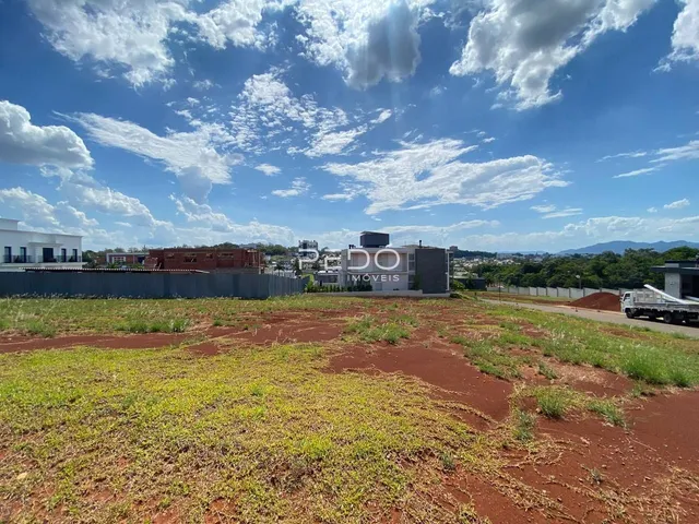 Vista aérea de um terreno aberto com vegetação rasteira e edifícios ao fundo.