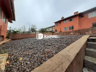 Vista externa de um quintal com cascalho e um muro de concreto em frente a uma casa.