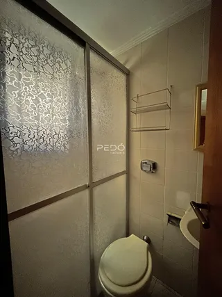 Banheiro com revestimento de azulejos claros e divisória de vidro.