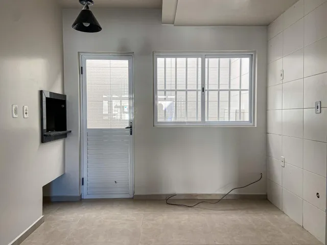 Uma sala de estar clara com uma janela e televisão montada na parede.