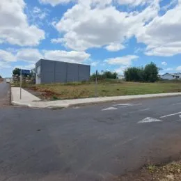 Fachada de um prédio com área de terra e estrada no primeiro plano.