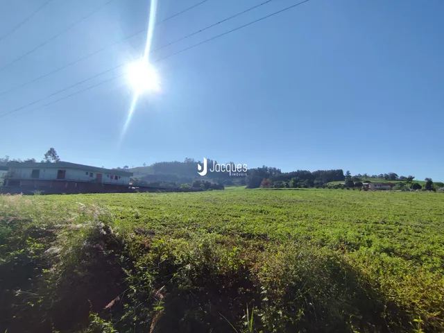 Vista de campos verdes e vegetação sob um céu azul em uma paisagem rural.