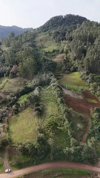 Vista aérea de uma paisagem montanhosa verde com campos cultivados e uma estrada de terra.