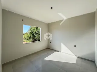 Ambiente interno de uma sala com piso de cerâmica e janela para a vegetação.