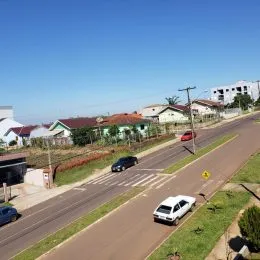 Vista de uma rua residencial em Lajeado, Brasil, com casas ao fundo sob um céu azul.