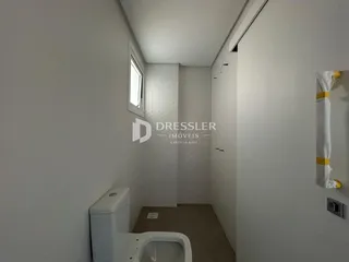 Vista de um corredor interno com parede branca e um vaso sanitário.