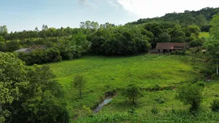 Vista aérea de uma área rural com campo verde e vegetação densa ao fundo.