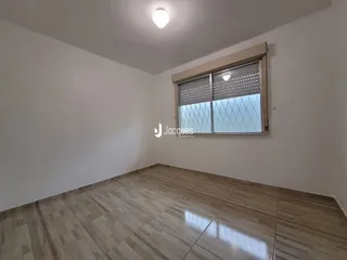 Vista interna de uma sala com piso de madeira clara e parede branca.