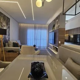 Uma sala de estar moderna com cortinas claras e iluminação natural.