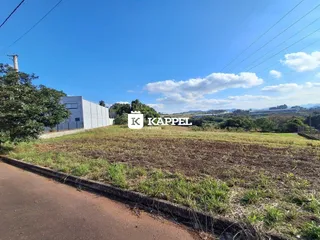 Vista panorâmica de uma área aberta com campo e um edifício ao fundo sob um céu azul.