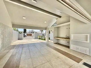 Área externa pavimentada com piso de cerâmica e paredes brancas de uma residência.