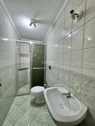 Banheiro com revestimento cerâmico e box de vidro.