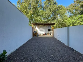 Vista externa de um quintal com parede branca e estrutura de madeira.