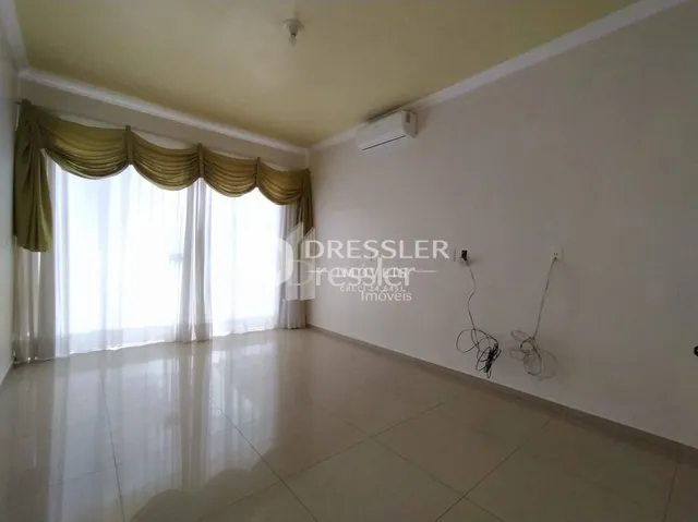 Ambiente interno com grandes janelas cobertas por cortinas claras.